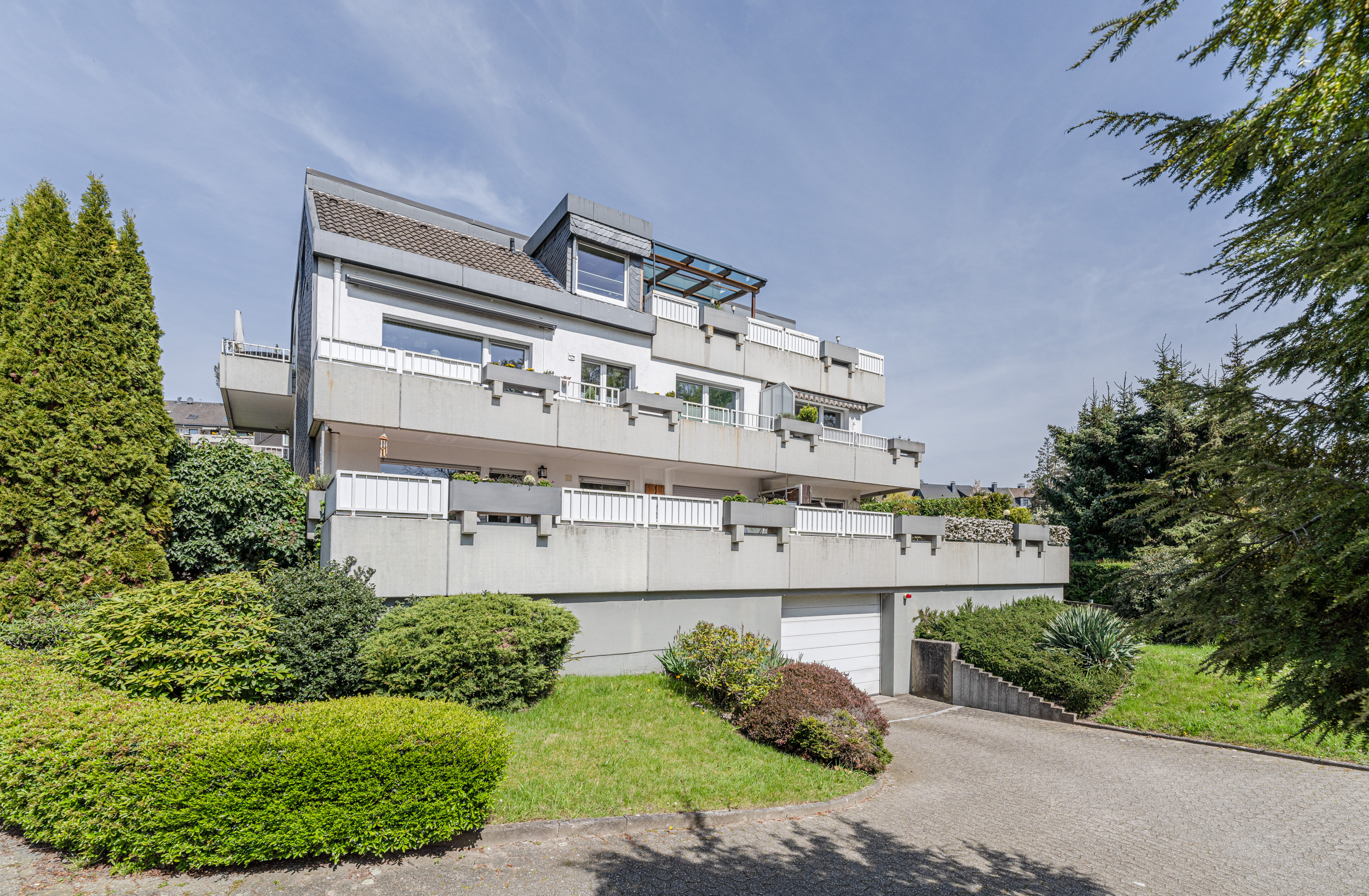 Mehrfamilienhaus mit großen Balkonen, Garage und grünem Vorgarten bei Sonnenschein.