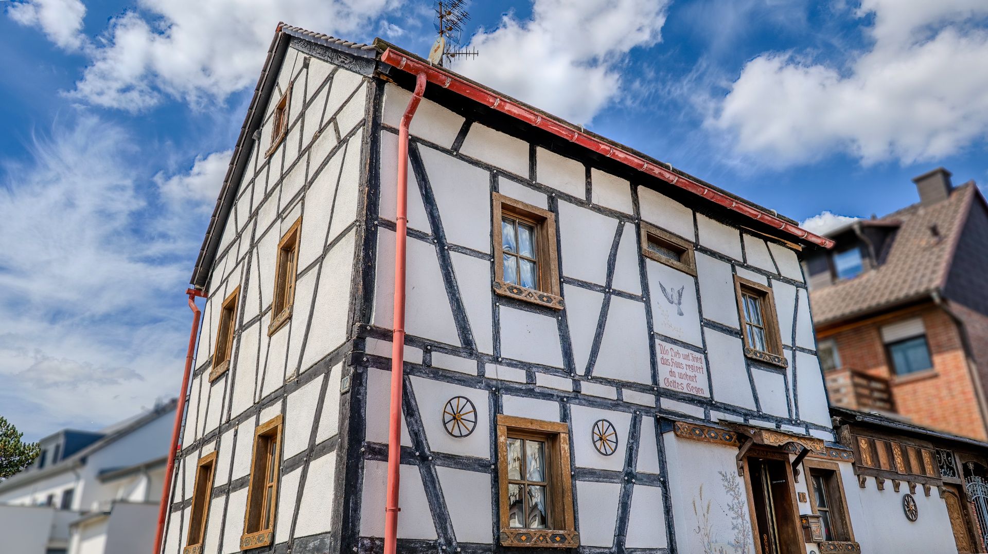 Fachwerkhaus mit weißen Wänden, schwarzen Balken und braunen Holzfenstern.