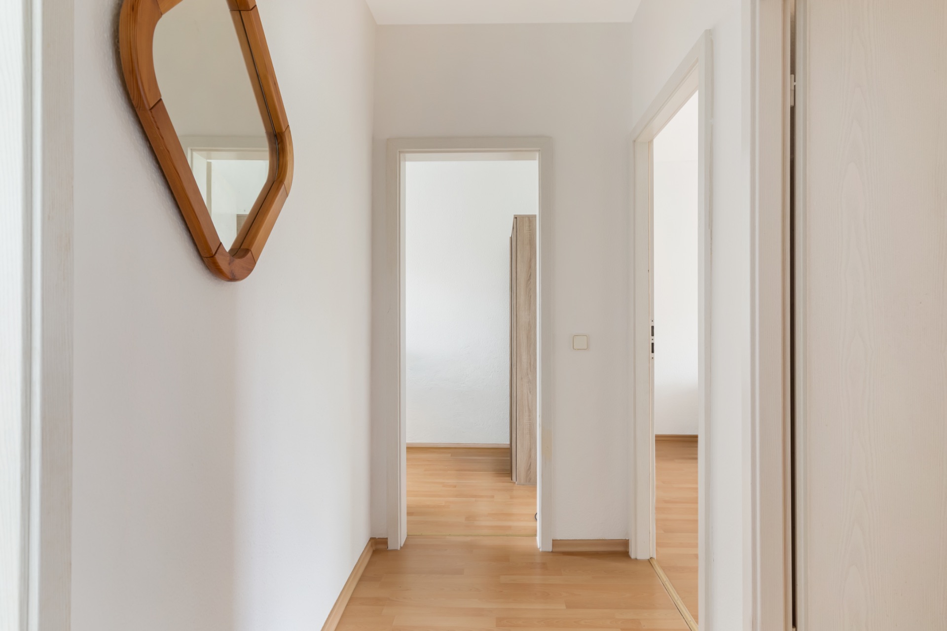 Heller Flur mit Holzspiegel an der Wand und Türen zu mehreren Räumen.