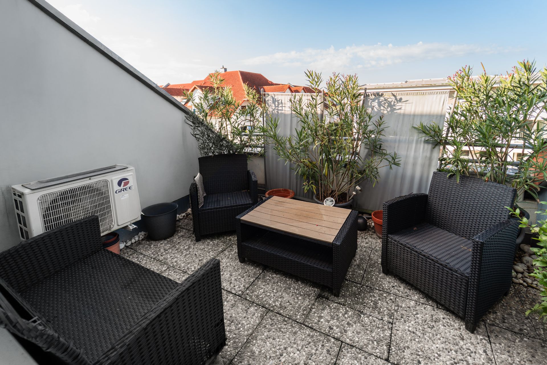 Kleine Terrasse mit vier schwarzen Stühlen, einem Tisch, Pflanzen und Klimagerät.