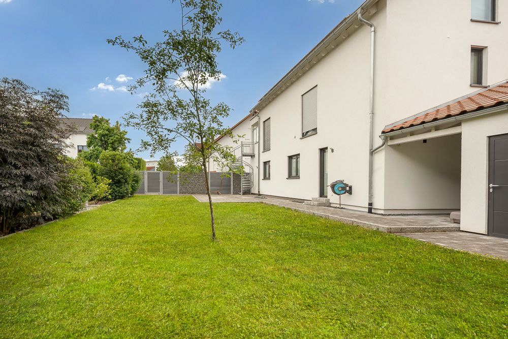 Grüner Garten mit Rasen und jungem Baum neben modernem Wohnhaus.