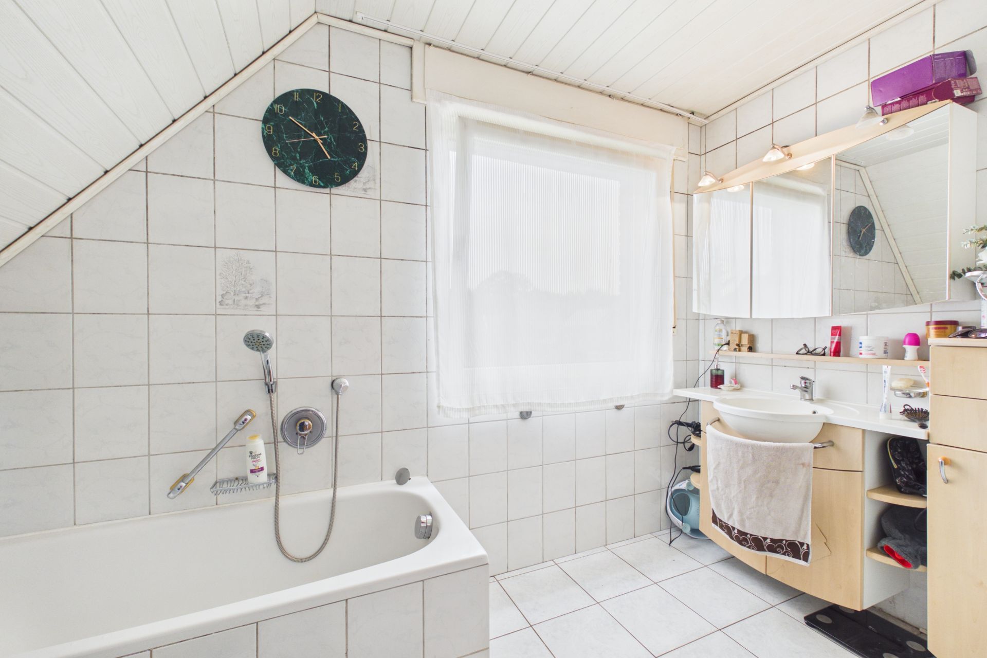 Helles Badezimmer mit Badewanne, großem Fenster, Waschbecken und Spiegel.