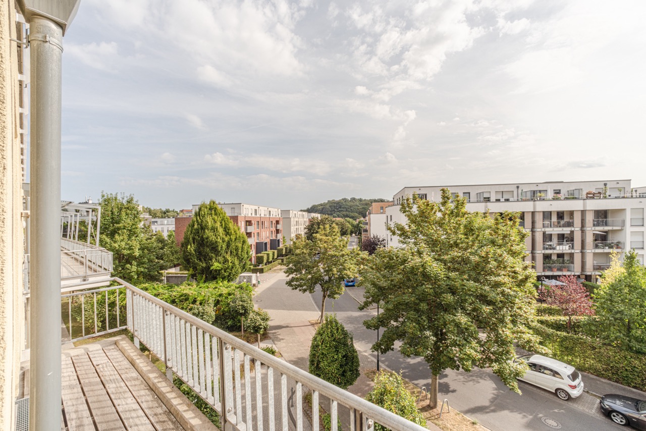 Blick von einem Balkon auf eine ruhige Wohnstraße mit Bäumen und modernen Wohnhäusern.