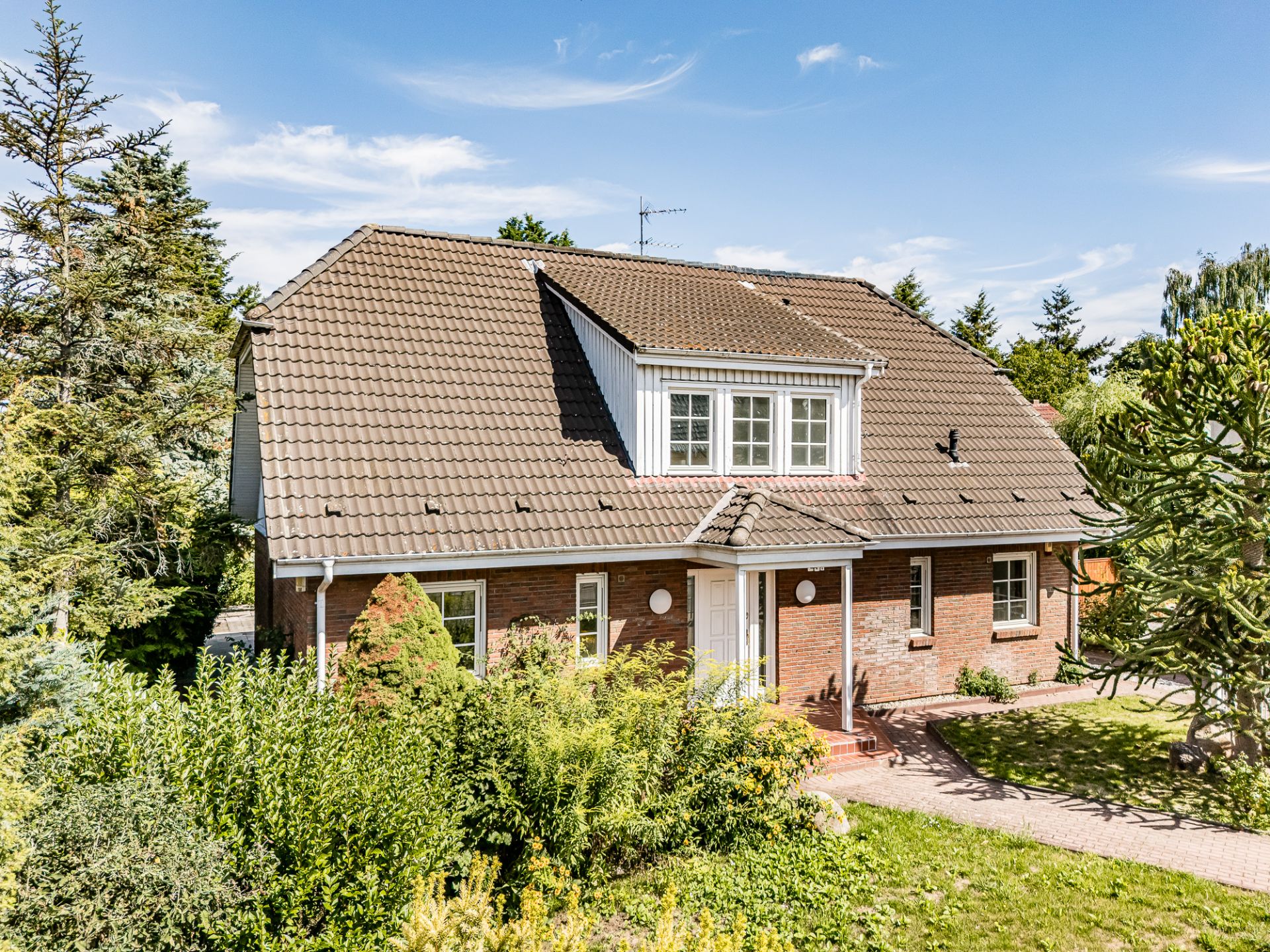 Backsteinhaus mit Satteldach, Eingangsbereich und Garten im Vordergrund an einem sonnigen Tag.