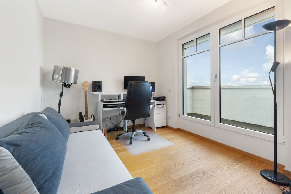 Arbeitszimmer mit Schreibtisch, Bürostuhl, Sofa und großer Fensterfront.