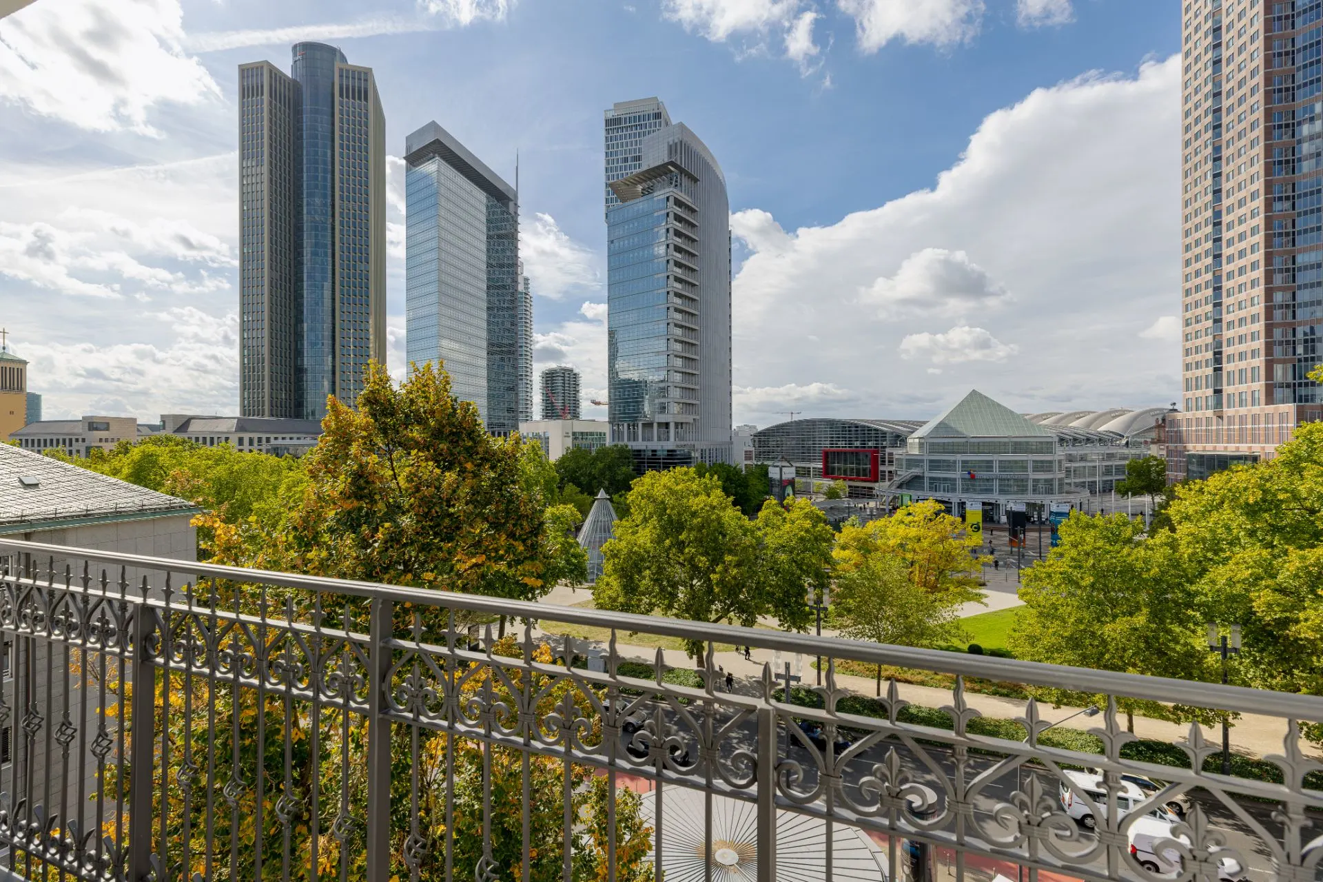 Blick von einem Balkon auf moderne Hochhäuser und Bäume in einer Stadt.