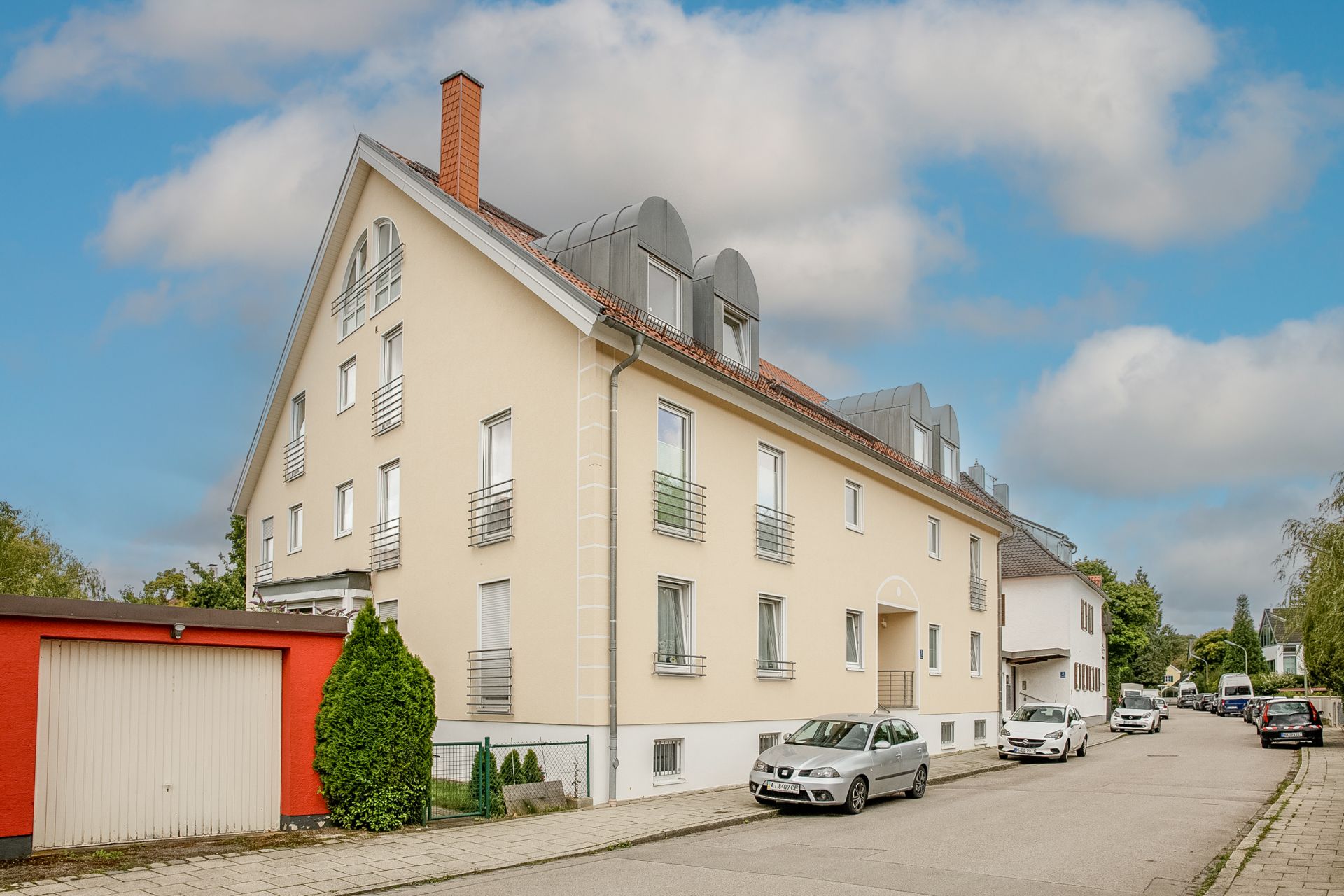 Mehrfamilienhaus mit hellgelber Fassade und geparkten Autos an einer ruhigen Wohnstraße.