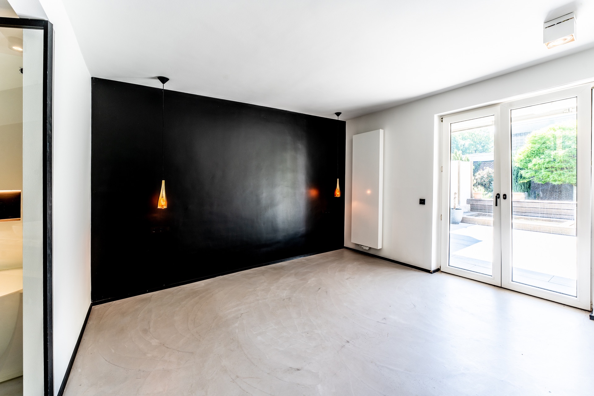 Leerer, moderner Raum mit schwarzer Wand, Hängelampen und großen Glastüren zum Garten.
