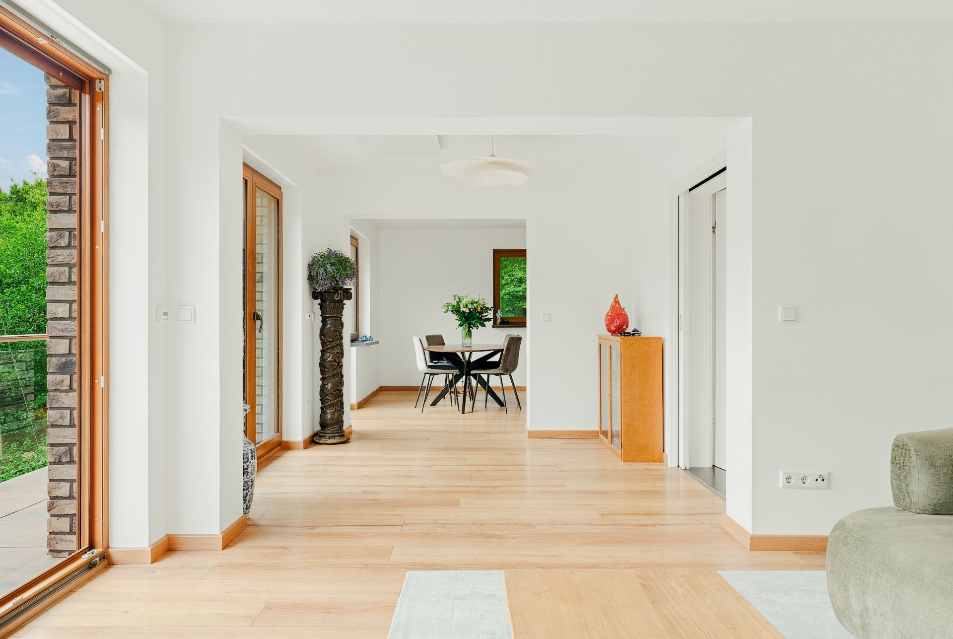 Heller Wohnraum mit Holzboden, großen Fenstern und einem Essbereich mit Tisch und Stühlen.