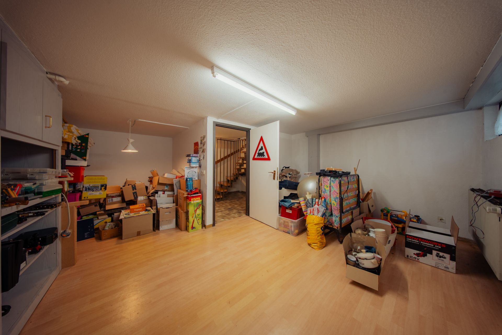 Kellerraum mit Holzboden, vielen Kartons und einer offenen Tür zu einer Treppe.