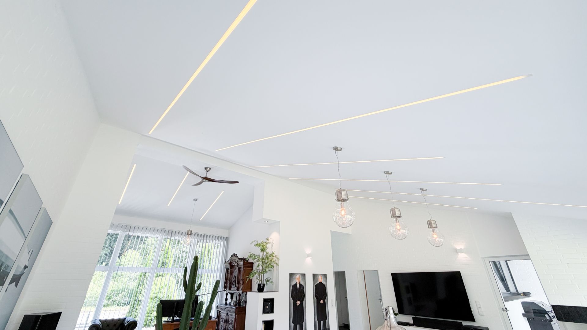 Modernes Wohnzimmer mit weißen Wänden, großen Fenstern und Hängelampen an der Decke.
