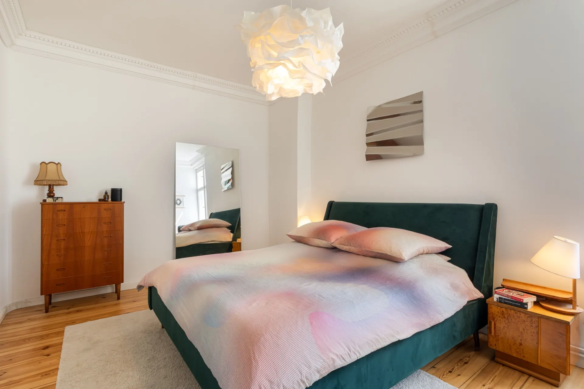 Helles Schlafzimmer mit Doppelbett, Nachttischlampen, Spiegel und Kommode auf Holzboden.