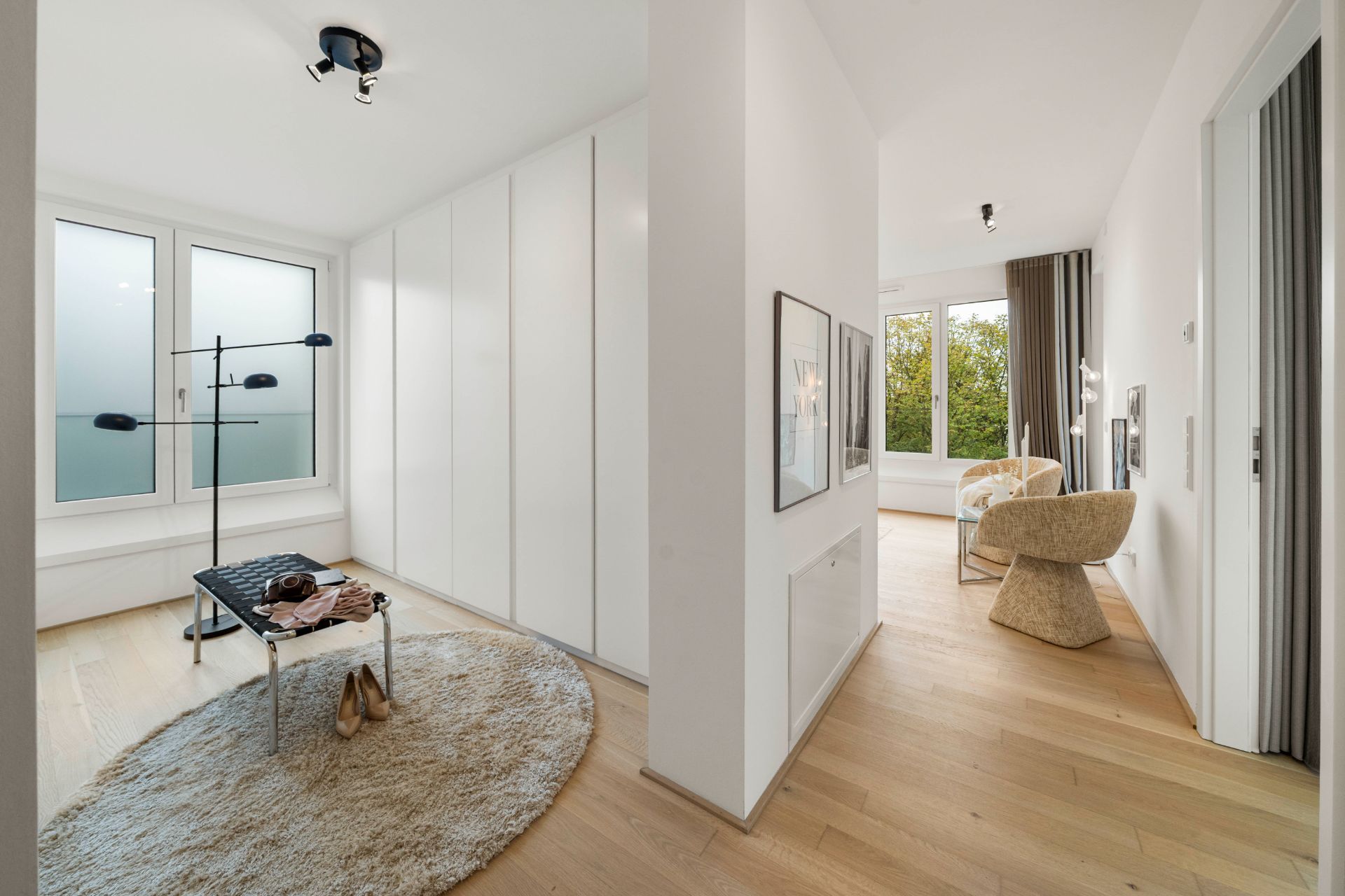 Heller Flur mit Einbauschränken, Teppich, Kleiderständer und Blick in ein Zimmer mit Sessel.