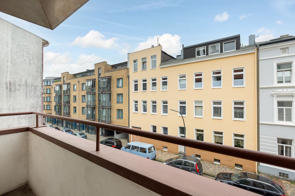 Blick von einem Balkon auf eine ruhige Straße mit mehreren mehrstöckigen Wohnhäusern.