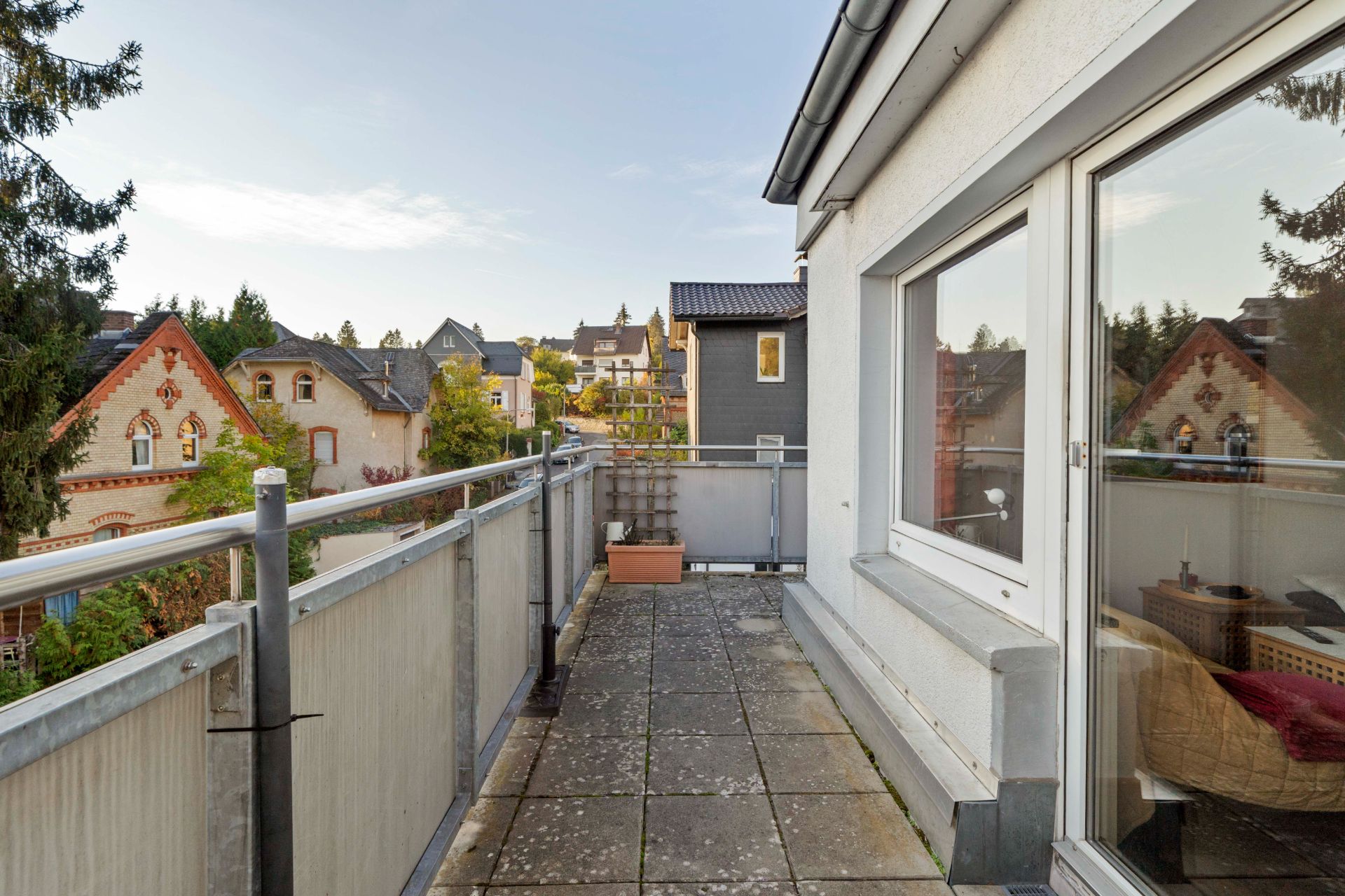 Balkon mit Fliesenboden, Geländer und Blick auf Nachbarhäuser und grüne Bäume.