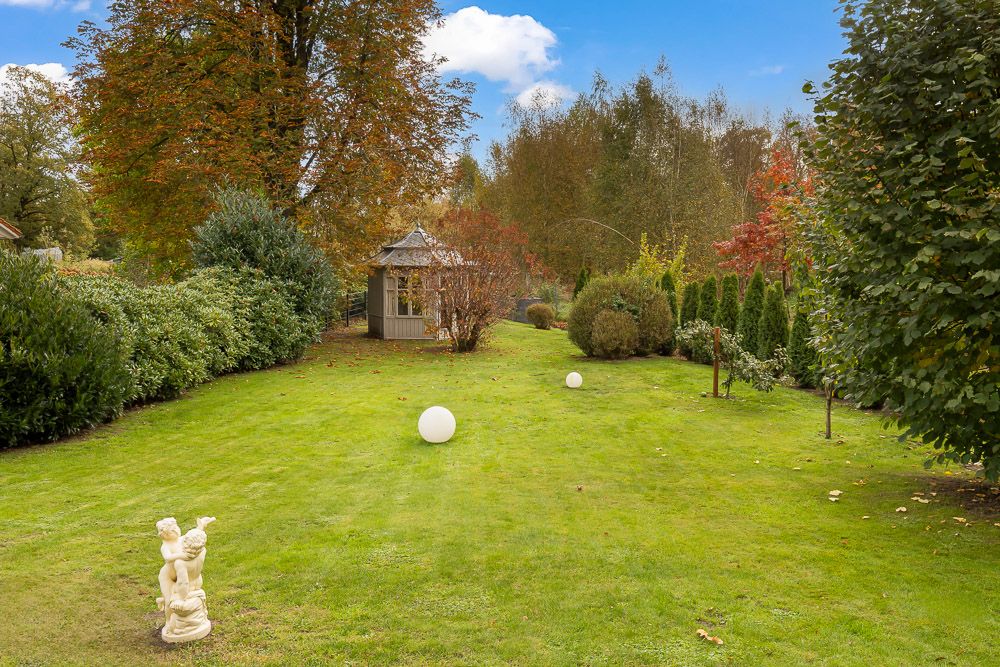 Großer Garten mit Rasen, Skulptur, weißen Kugeln und kleinem Pavillon im Hintergrund.