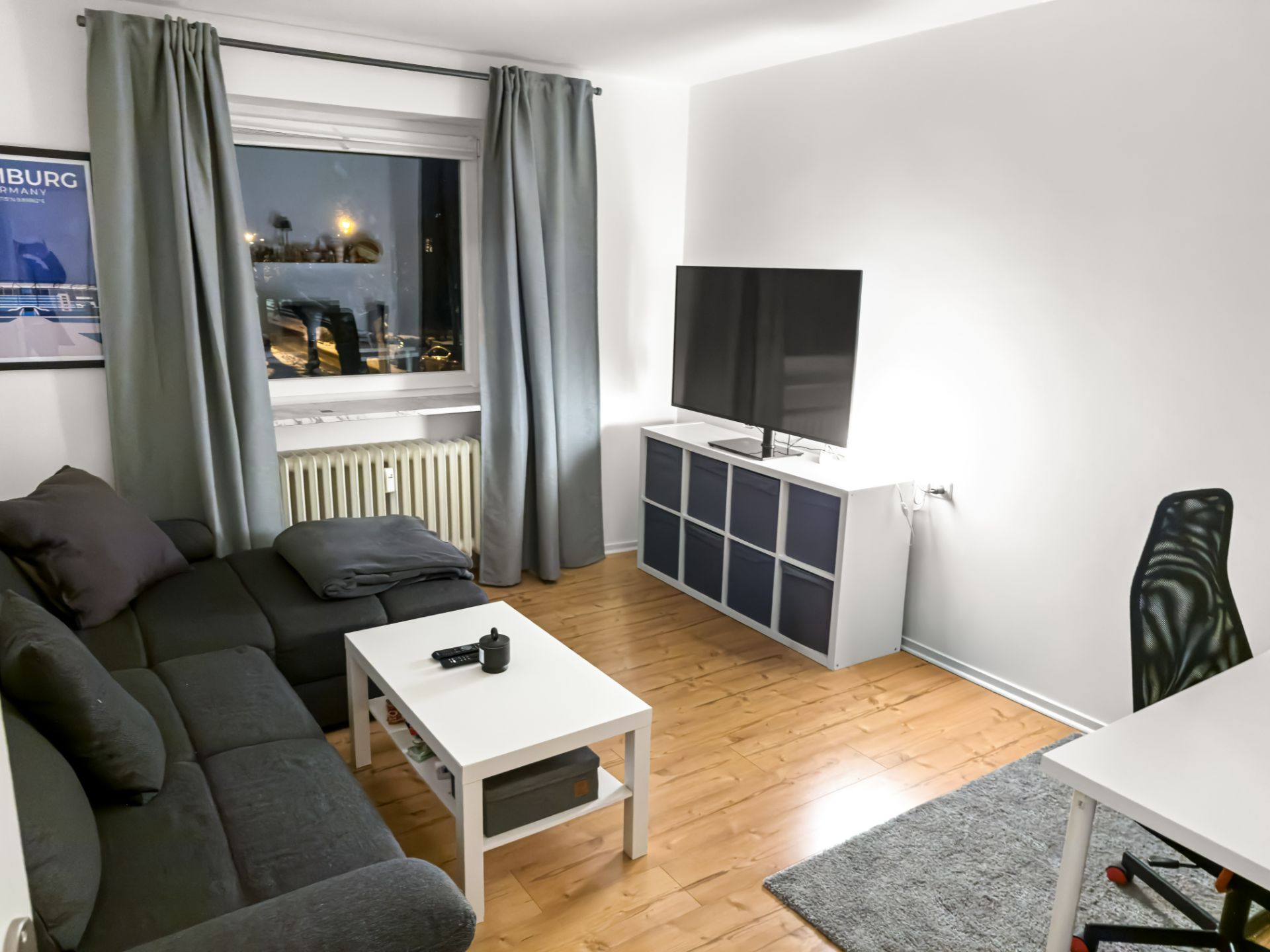 Modernes Wohnzimmer mit grauem Sofa, Couchtisch, Fernseher und Schreibtisch auf Holzfußboden.
