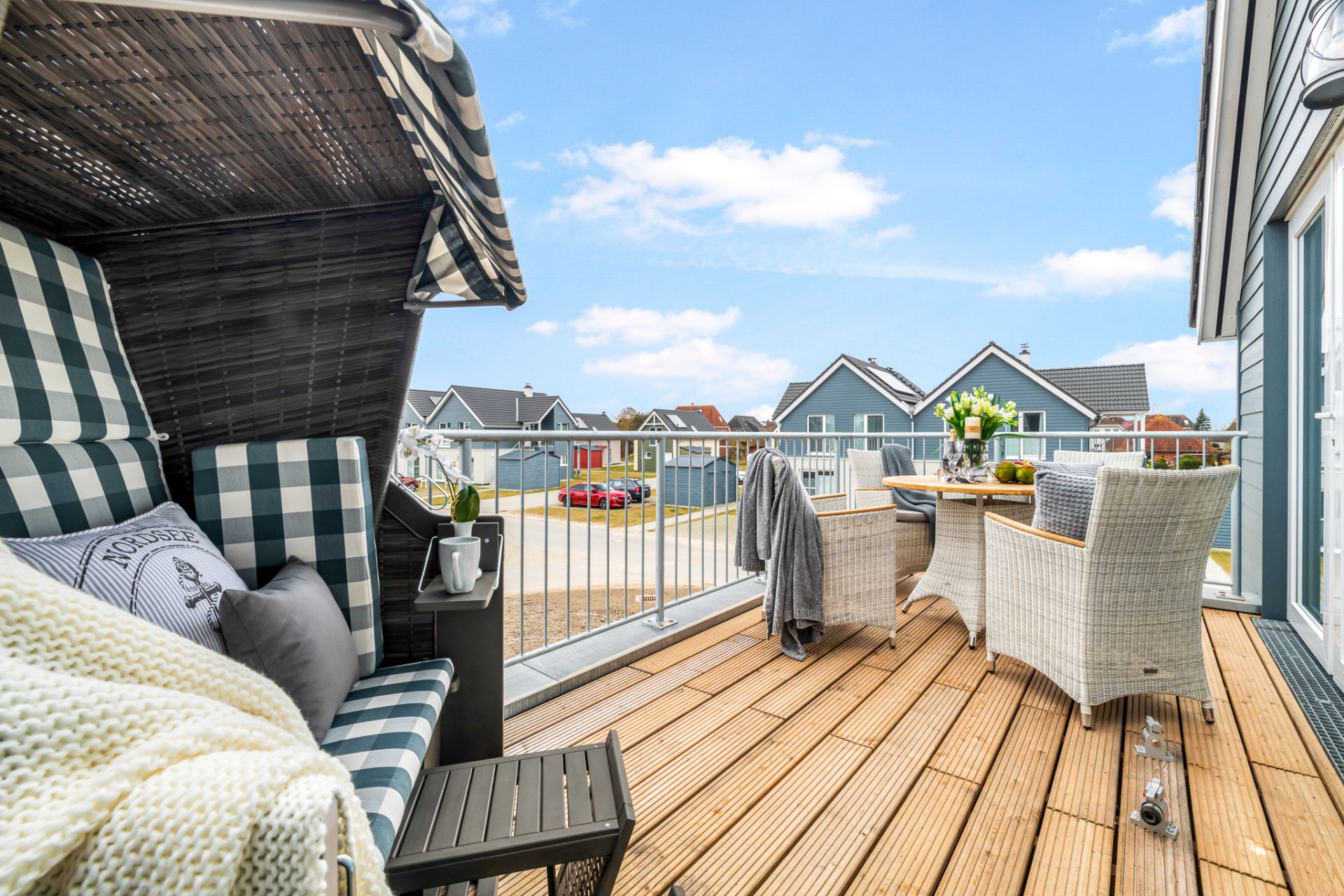 Balkon mit Sitzbank, Esstisch und zwei Korbstühlen, Blick auf Nachbarhäuser.
