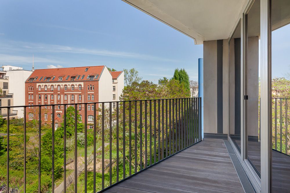 Moderner Balkon mit Glasgeländer und Blick auf einen Garten und ein rotes Wohngebäude.