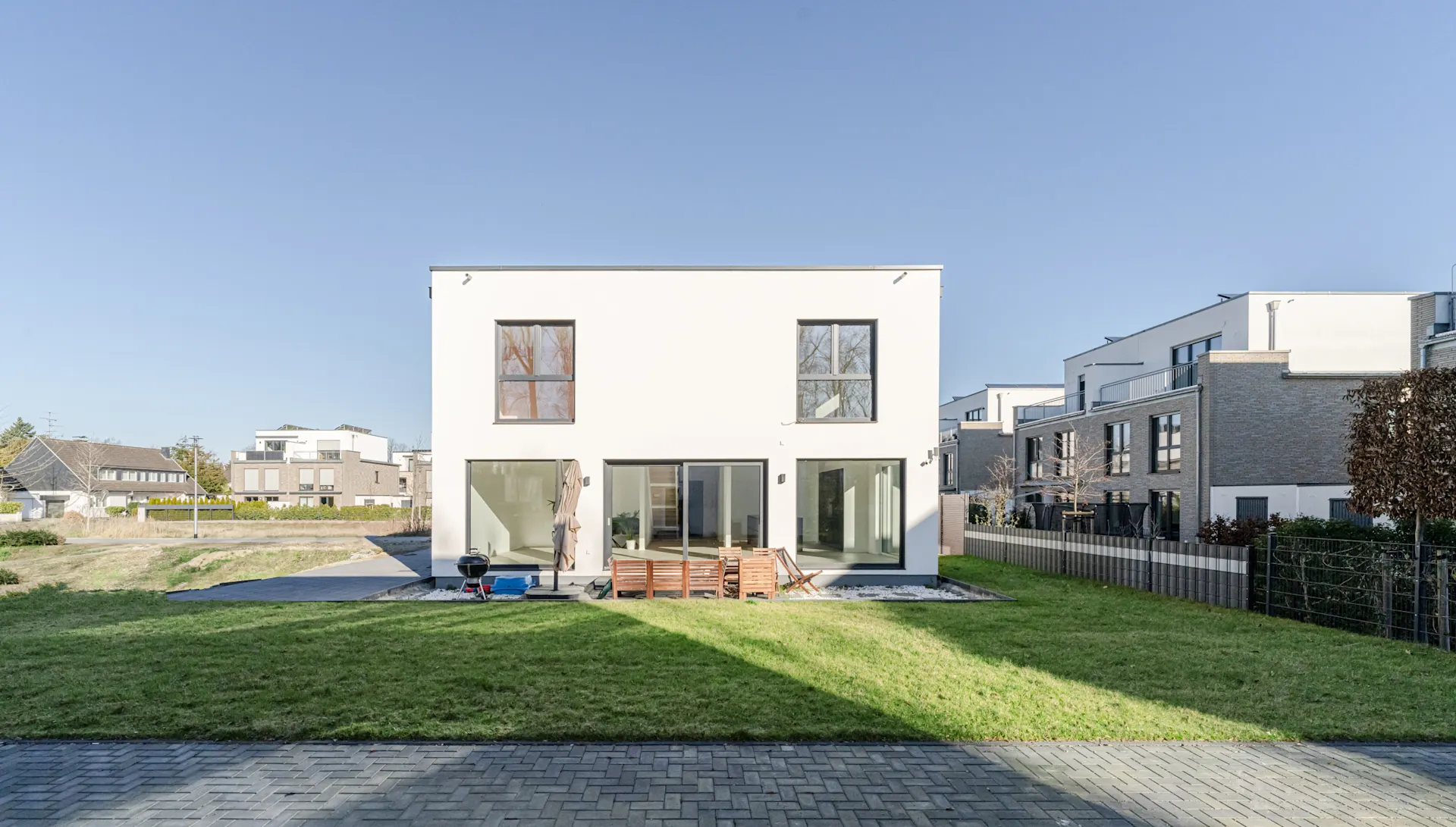 Modernes, zweistöckiges weißes Wohnhaus mit großen Fenstern und Garten im Vordergrund.