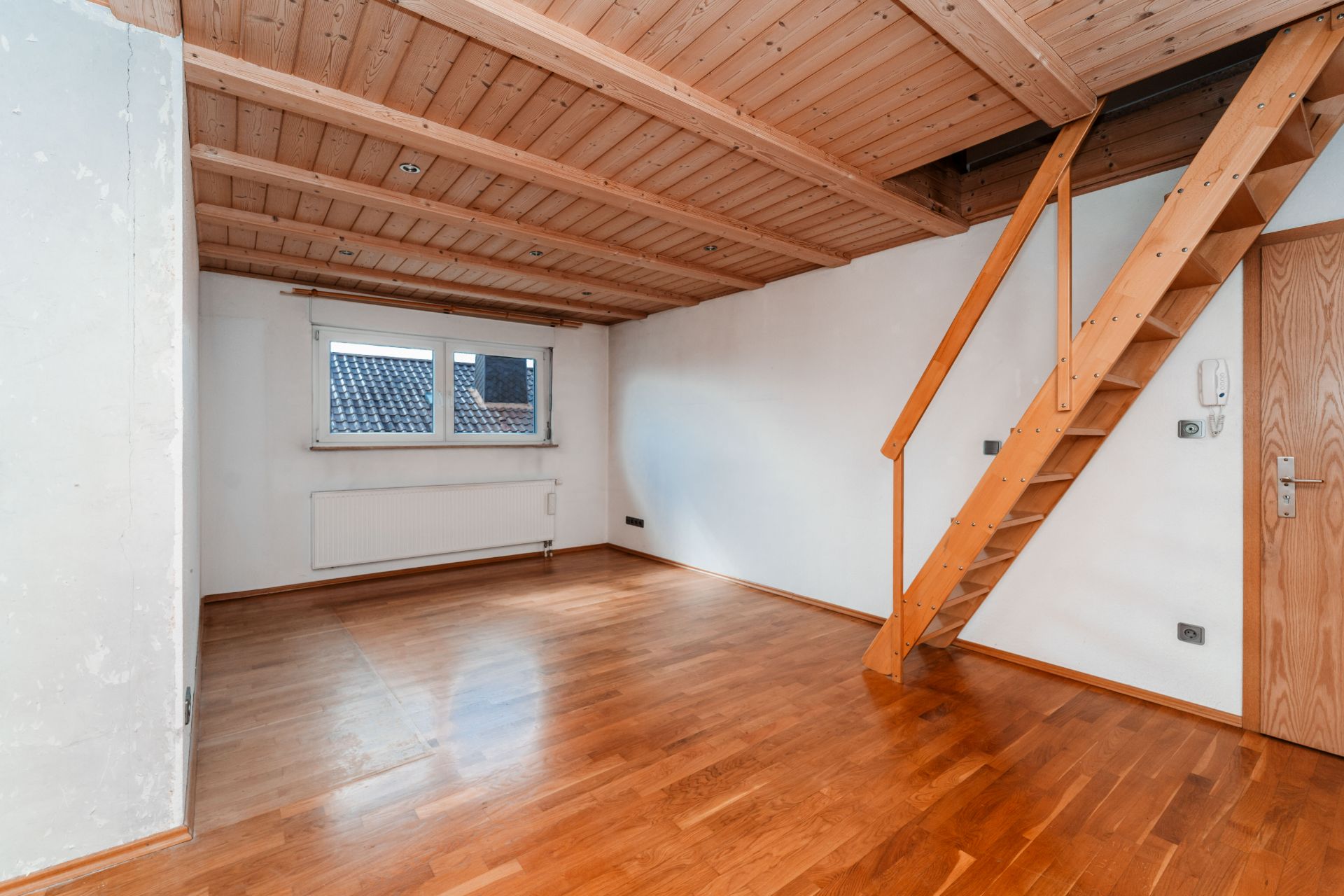 Leeres Zimmer mit Holzboden, Holzdecke, Fenster und Holztreppe zur Empore.