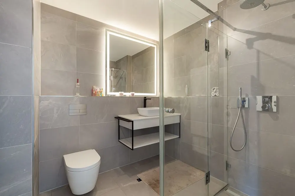 Modernes Badezimmer mit großer Dusche, WC, Waschbecken und beleuchtetem Spiegel.