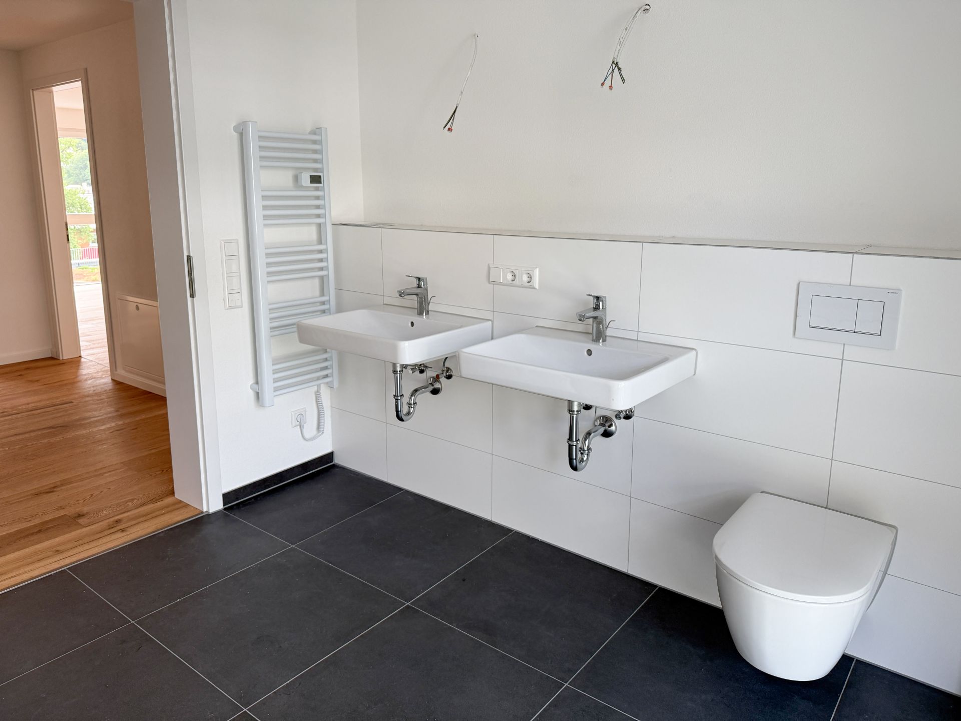 Modernes Badezimmer mit zwei Waschbecken, Wandtoilette und Handtuchheizkörper.