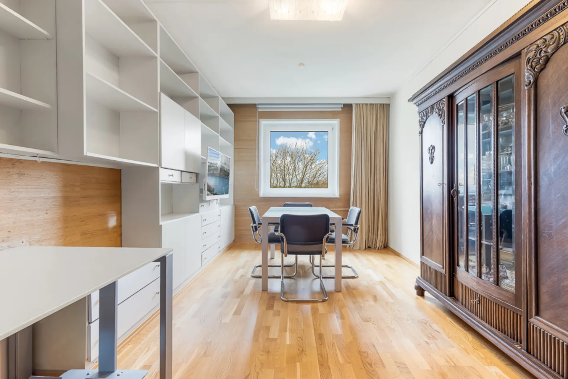 Heller Raum mit Esstisch, vier Stühlen, modernen Regalen und großem Holzschrank.