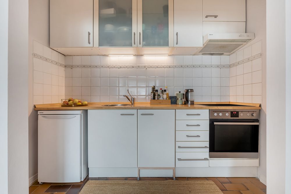 Moderne Einbauküche mit weißem Kühlschrank, Herd, Spüle und Oberschränken.