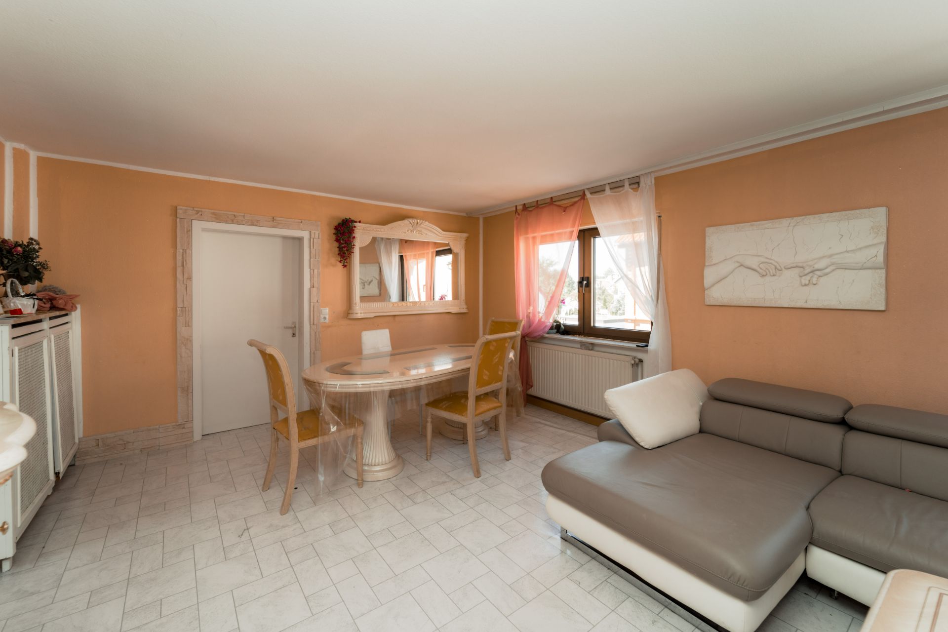 Wohnzimmer mit Ecksofa, Esstisch und Stühlen, helle Fliesen und orangenfarbene Wände.