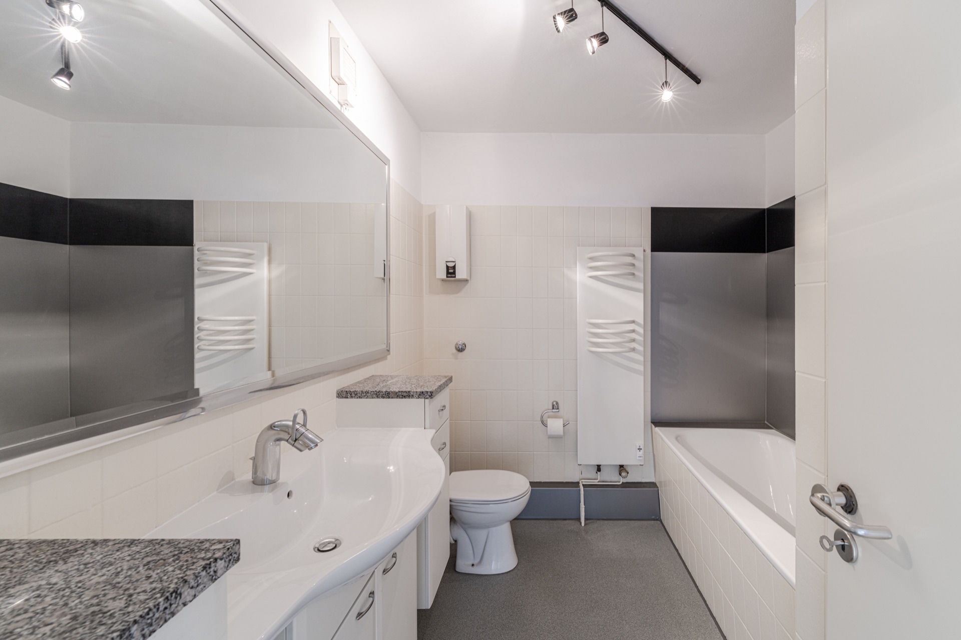 Modernes Badezimmer mit großem Spiegel, Waschbecken, Toilette, Handtuchheizkörper und Badewanne.