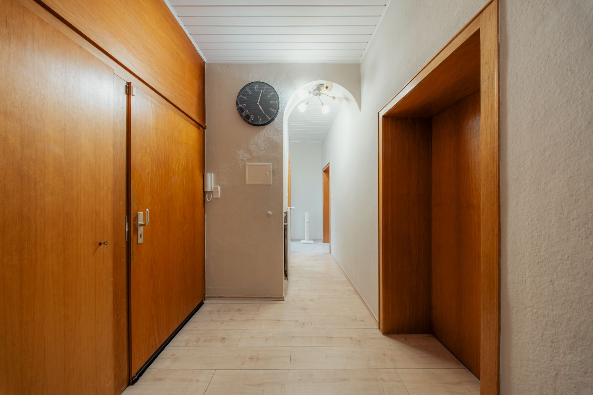 Flur mit Holzverkleidung, Wanduhr und hellen Fliesen, mehrere Türen führen in andere Räume.