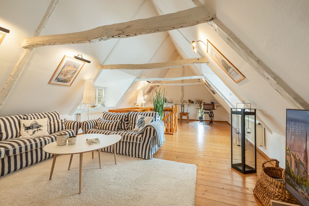 Helles Dachgeschoss-Wohnzimmer mit Holzbalken, gestreiften Sofas und einem ovalen Tisch.