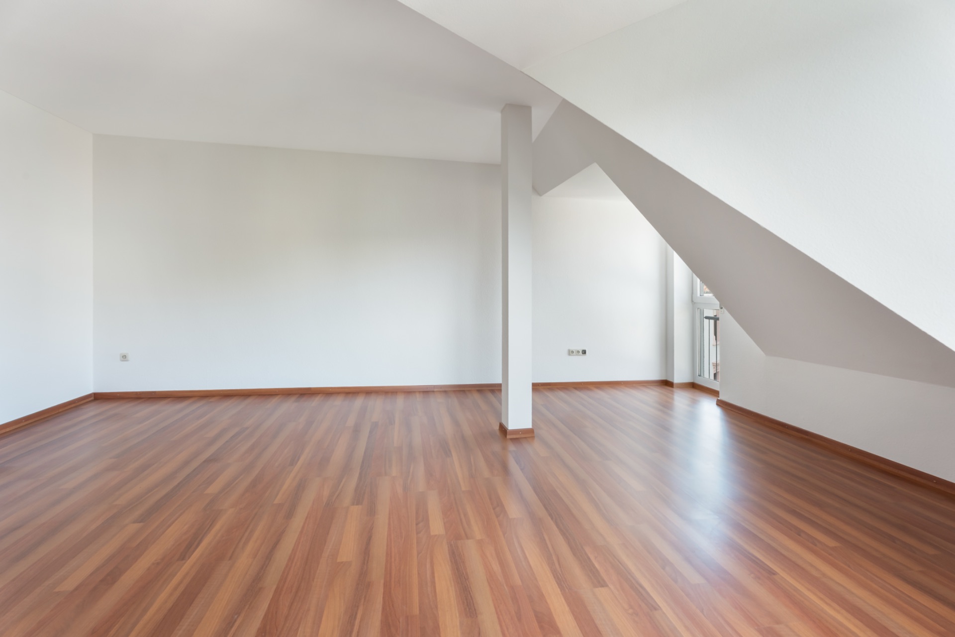 Leerer Raum mit weiß gestrichenen Wänden und Laminatboden, Dachschräge und Säule in der Mitte.