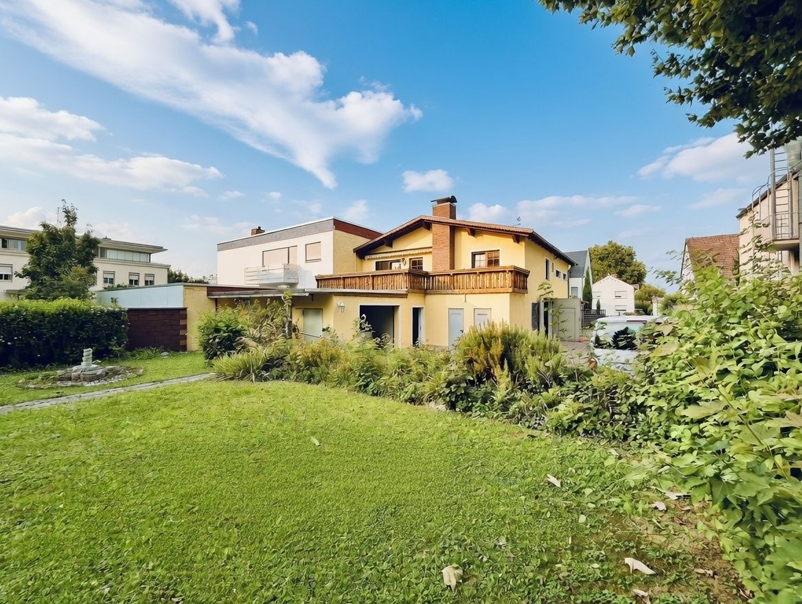 Gelbes Wohnhaus mit Balkon und großem Garten bei blauem Himmel.