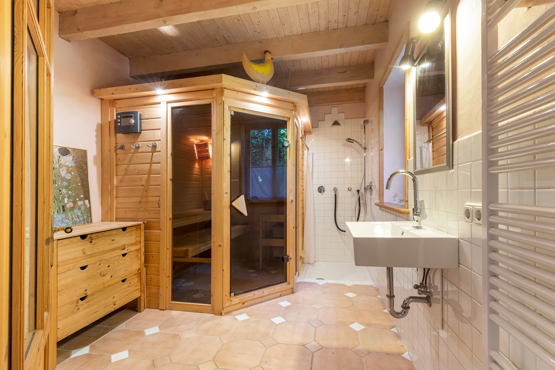 Helles Badezimmer mit Holzbalkendecke, Sauna, Dusche, Waschbecken und Holzkommode.