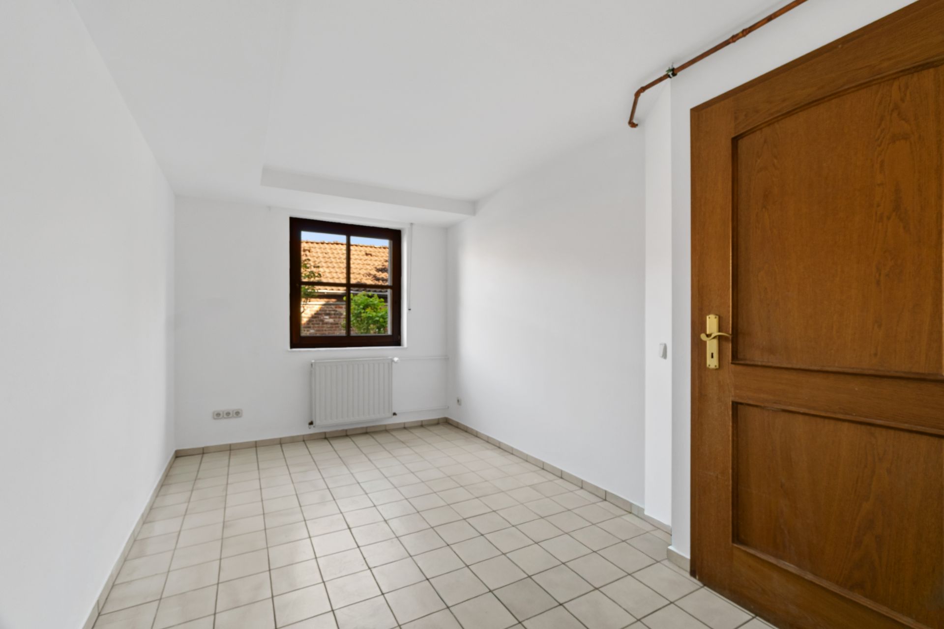 Leerer Raum mit weißen Wänden, Fliesenboden, Fenster und Holztür.