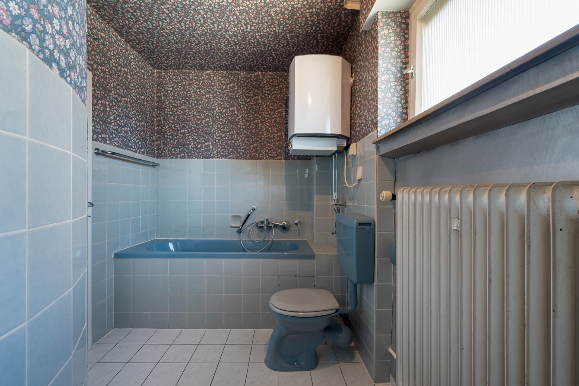 Kleines Badezimmer mit blauer Badewanne, Toilette, Wasserboiler und Heizung.