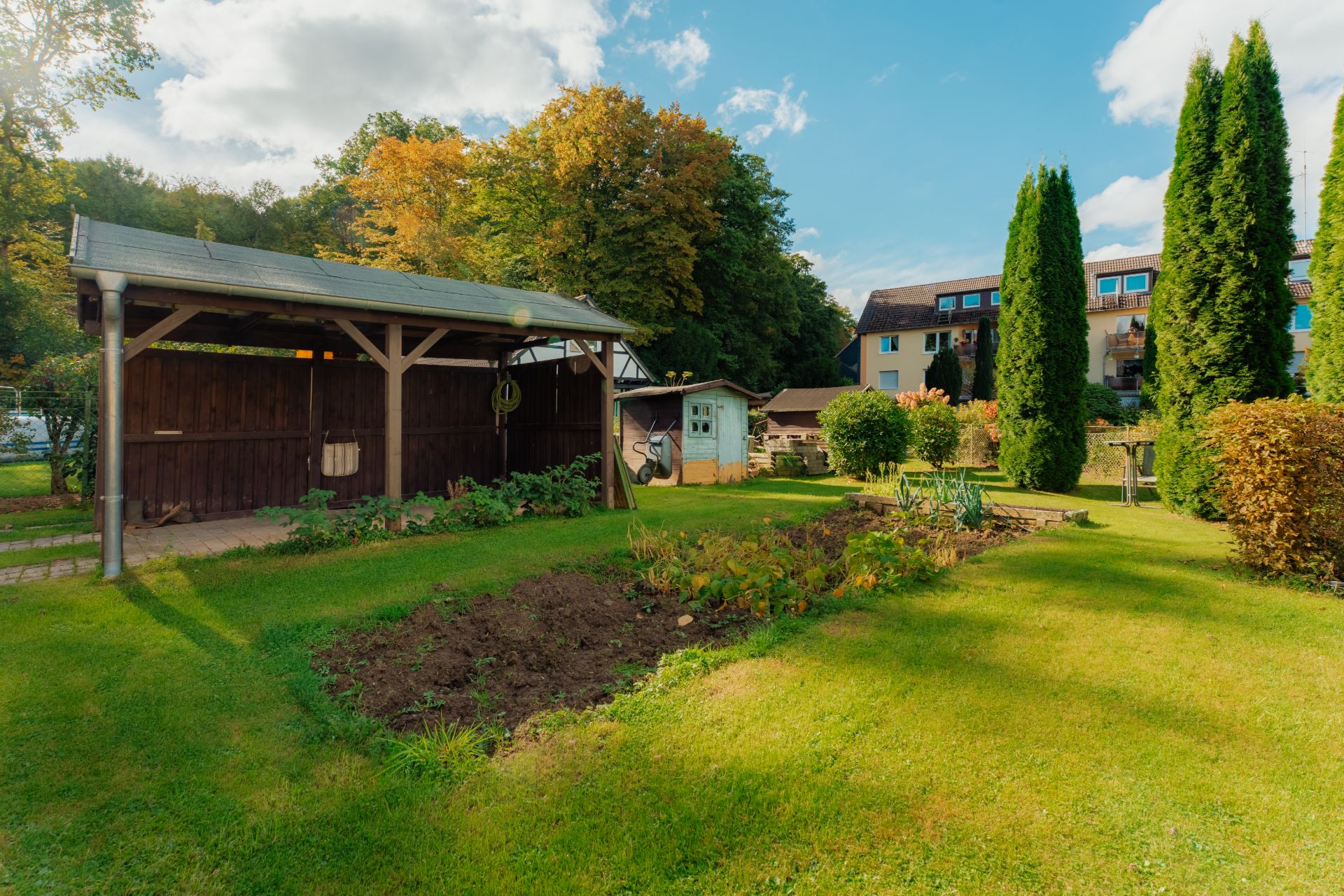 Gepflegter Garten mit Schuppen, Gemüsebeet, Bäumen und Rasenfläche bei Wohngebäuden.