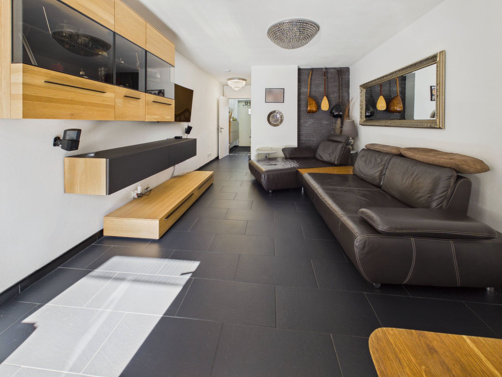 Modernes Wohnzimmer mit dunklen Fliesen, braunen Ledersofas und Holzmöbeln.