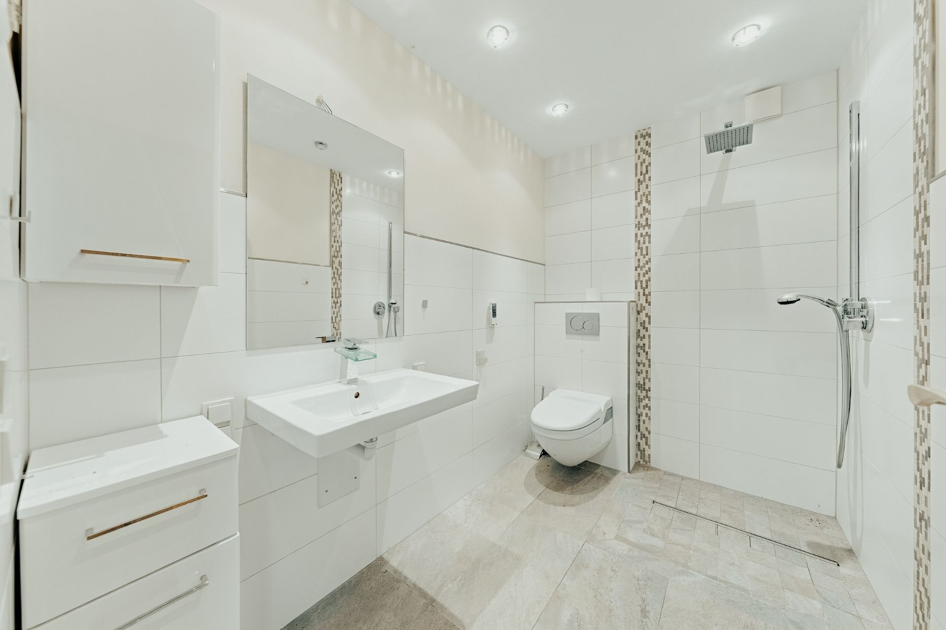 Helles, barrierefreies Badezimmer mit Dusche, WC, Waschbecken und weißen Fliesen.