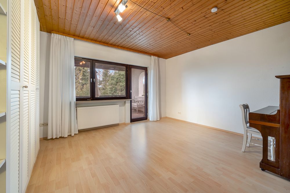 Helles Zimmer mit Holzdecke, großem Fenster, Vorhängen, Klavier und Stuhl auf Parkettboden.