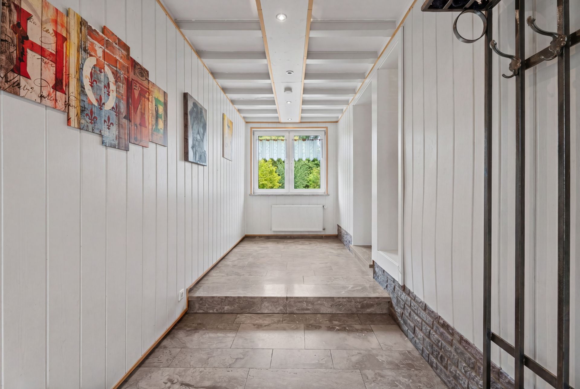 Heller Flur mit weißen Wänden, Kunst an der Wand und Fenster mit Blick ins Grüne.