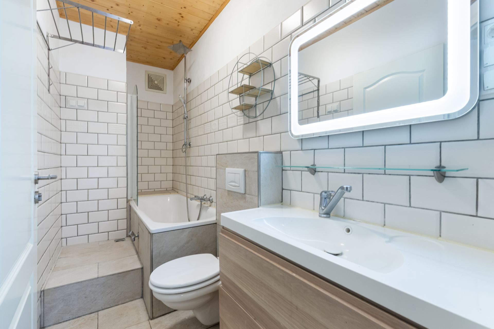 Modernes Badezimmer mit Badewanne, WC, Waschbecken und beleuchtetem Spiegel.
