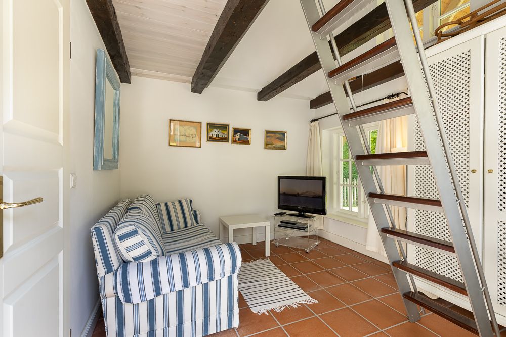 Wohnzimmer mit gestreiftem Sofa, Fernseher, Teppich und Treppe zu einer oberen Ebene.