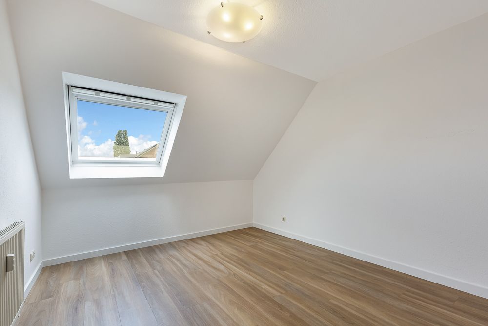 Helles Zimmer mit Dachschräge, großem Fenster und Holzfußboden.