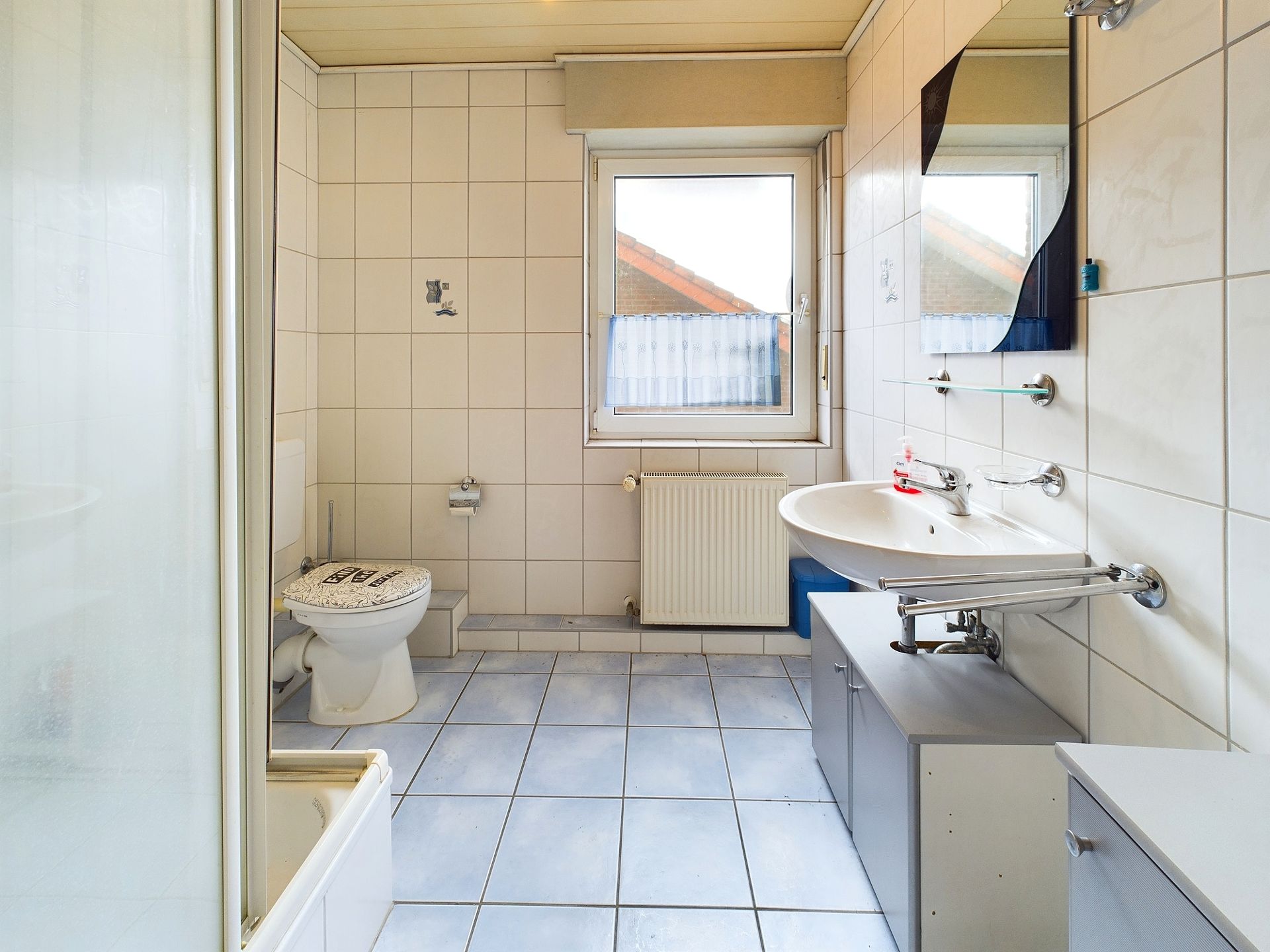 Helles Badezimmer mit Toilette, Waschbecken, Spiegel, Dusche und Fenster.