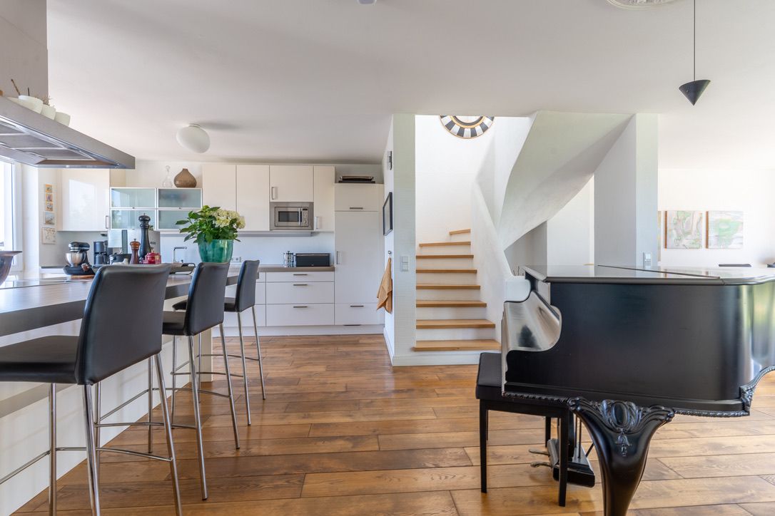 Moderne Küche mit Tresen, schwarzen Stühlen, Flügel und Treppe im Hintergrund.