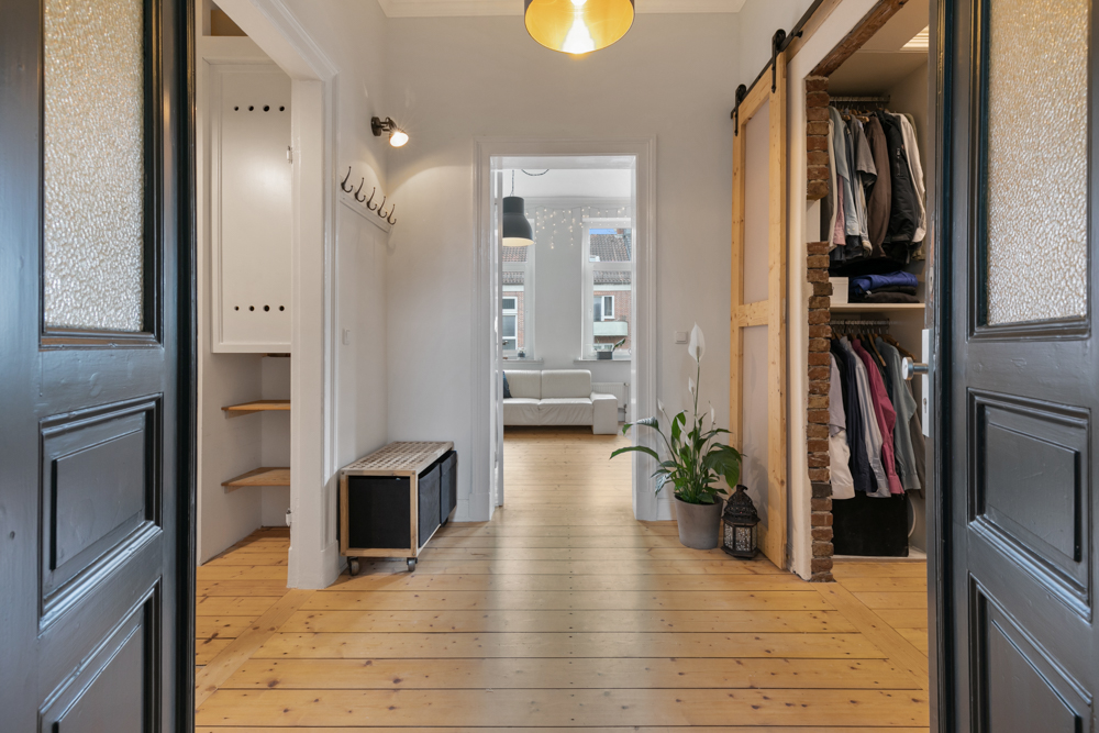 Heller Flur mit Holzboden, Garderobe, Sitzbank, Pflanze und offenem Kleiderschrank.
