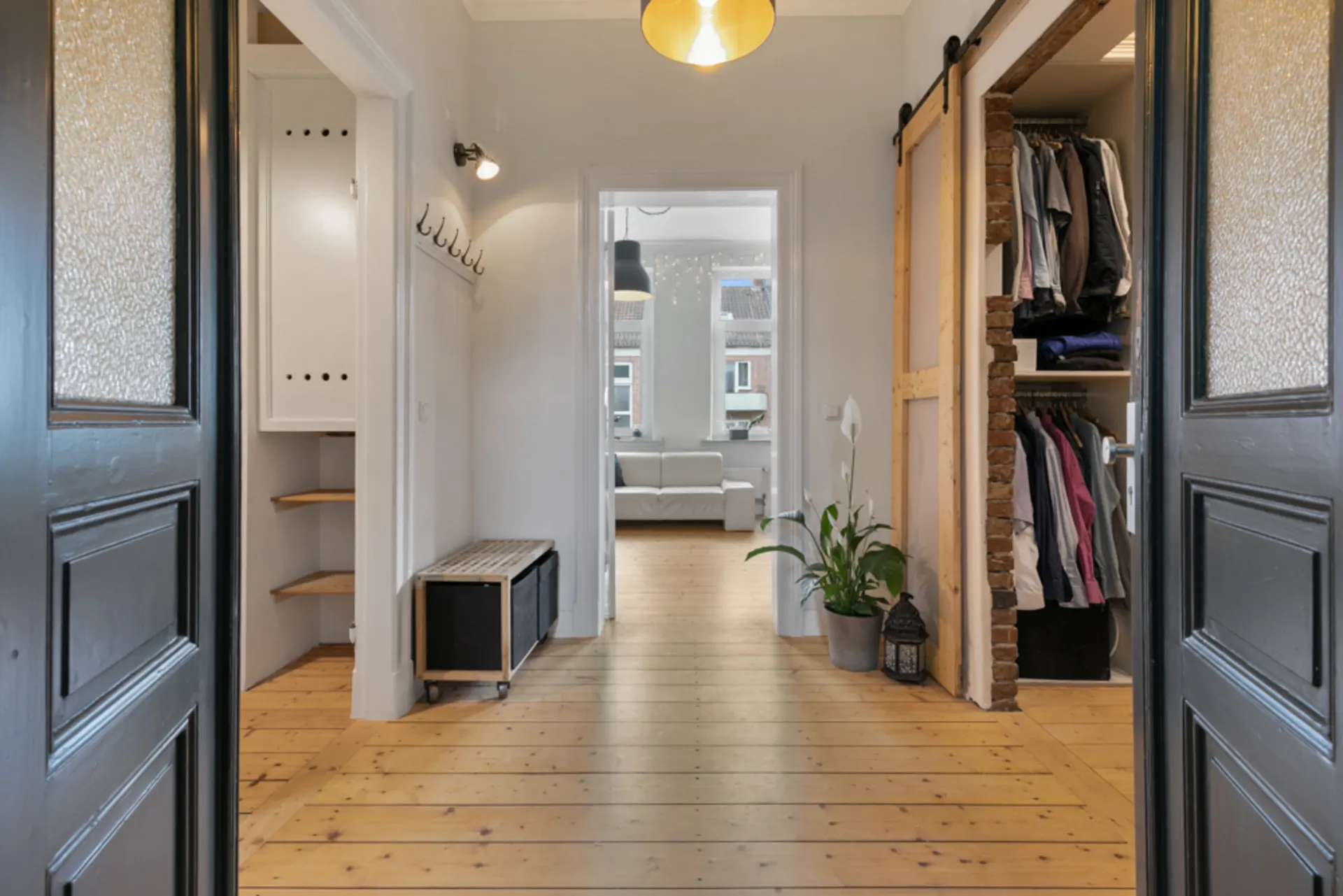 Heller Flur mit Holzboden, Garderobe, Sitzbank, Pflanze und offenem Kleiderschrank.